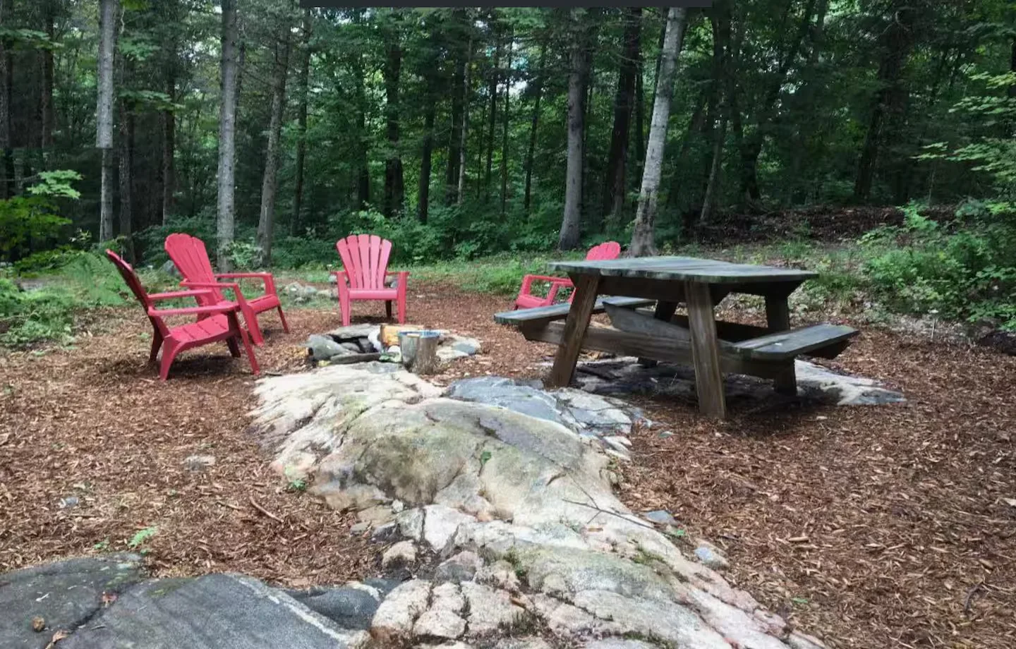 Fire pit area with red Adirondack chairs in the forest